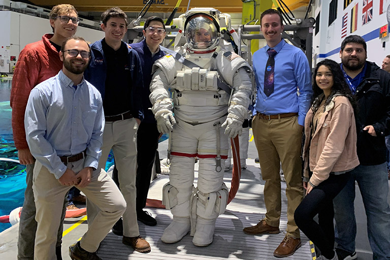 Miller McSwain and the group he worked with poses with former astronaut Rex Walheim in a space suit.