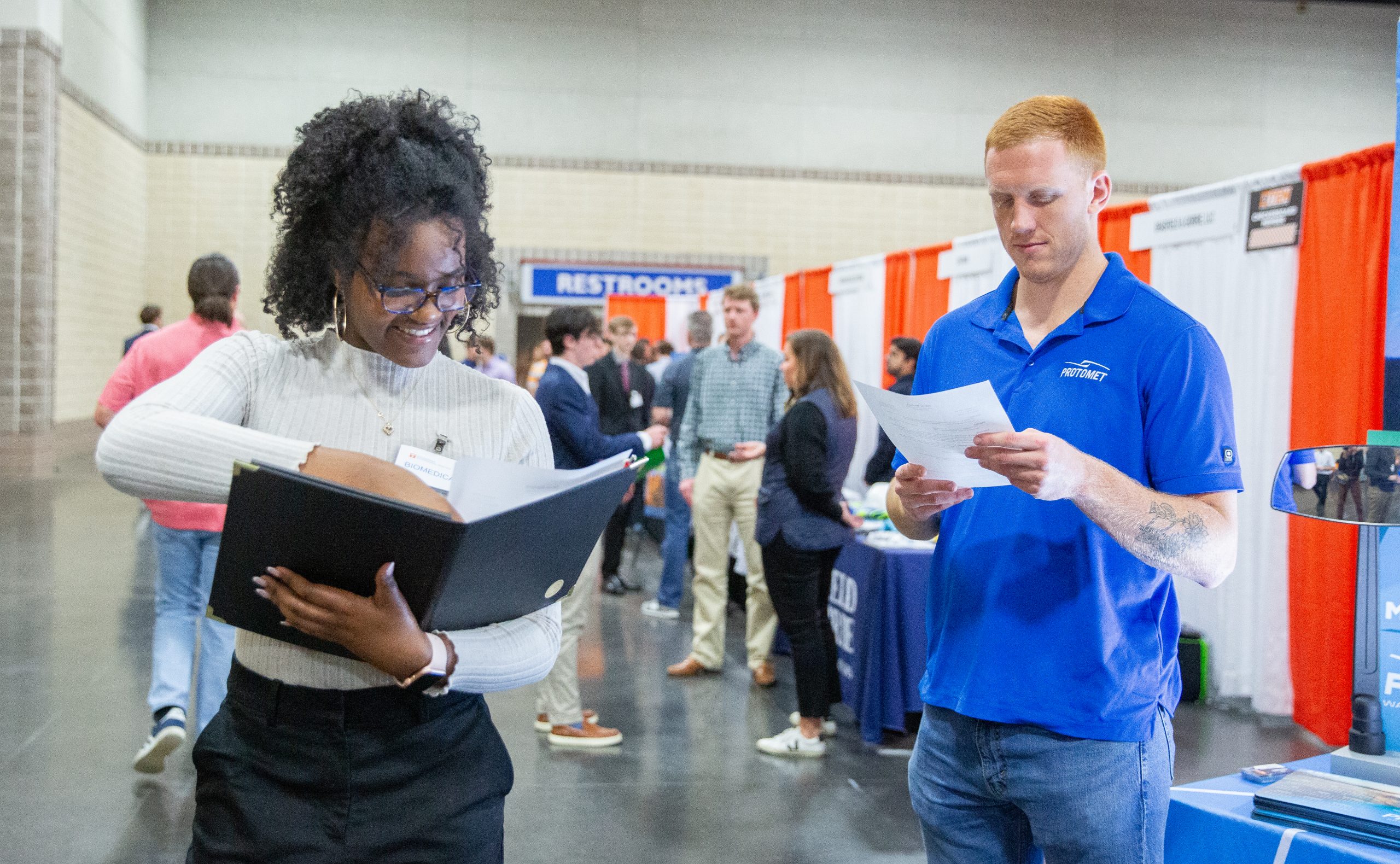 Female student giving her resume to a Protomet recruiter at the spring 2024 Engineering expo