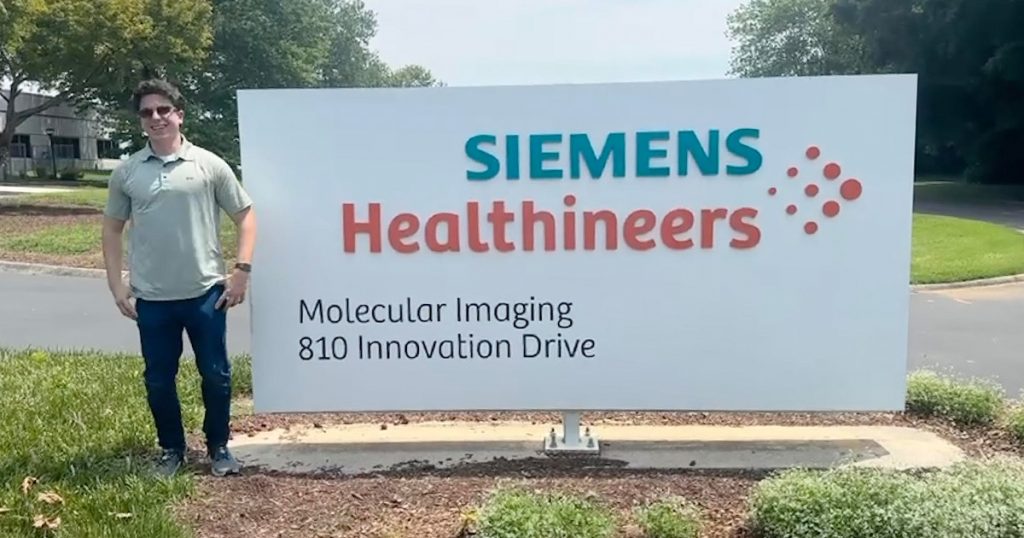 Logan Goodbred standing beside the Siemens Healthineers sign