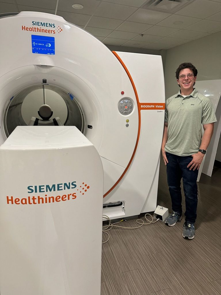 Logan Goodbred standing beside the Biograph Trinion PET/CT scanner